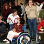 Das Foto zeigt eine Gruppe von Menschen, die in einem Theaterfoyers zusammenkommen und scheinbar an einer Vorstellung oder einem Event teilnehmen. Besonders hervorgehoben werden Personen im Rollstuhl, die mit anderen interagieren und Teil der Veranstaltung sind.