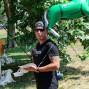 Ein Mann mit Sonnenbrille und T-Shirt hält eine weiße Schachtel in der Hand und lächelt in die Kamera. Im Hintergrund befindet sich ein großer, aufblasbarer Pferdekopf und eine Standfläche mit mehreren weißen kleinen Bauchten.