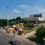 Auf dem Foto ist ein mehrstöckiges Gebäude mit einem hellen Dach und einer Treppe, vermutlich ein Kulturzentrum, in einer Stadt zu sehen. Um das Gebäude herum befinden sich Straßen, Feuerwehrautos und ein belebter öffentlicher Platz mit Fußgängern und Fahrzeugen.