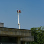Auf einem Gebäude mit einem Betonstüber steht ein Kran mit Personen auf einem Arbeitskorb. Der Himmel ist blau und es ist ein sonniger Tag.