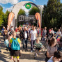 Viele Menschen strömen an einem sonnigen Tag durch einen Eingangsbogen zu einer Veranstaltung der „Trickfabrik Schwedt e.V.“. Rundherum stehen Bäume, Stände und Werbebanner, während Besucher mit Kindern, Fahrrädern und Rucksäcken unterwegs sind.